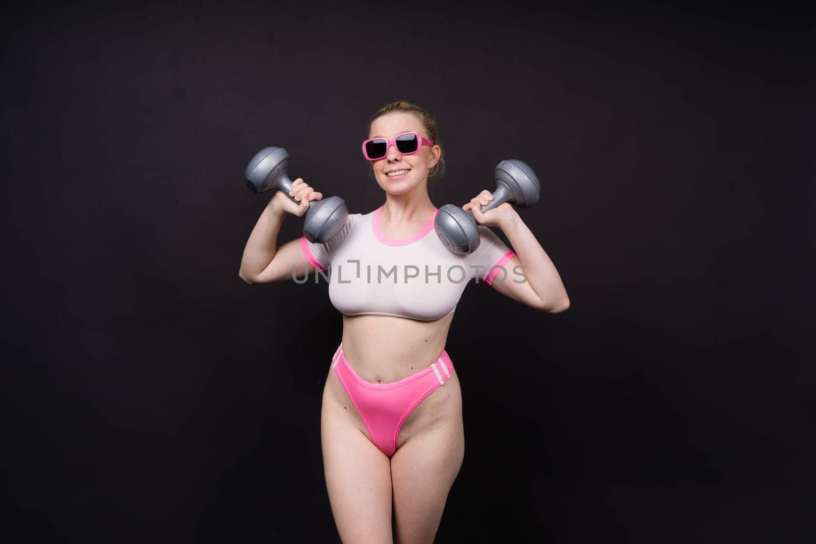 Seductive beautiful fitness female, athletic woman working out with dumbbells. Isolated in a studio