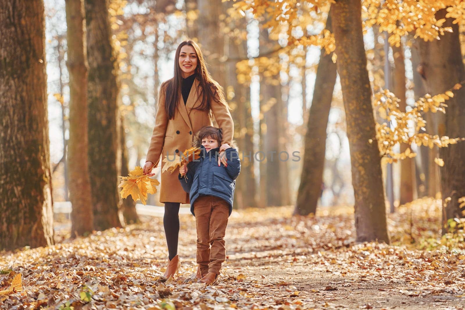 Front view. Mother with her son is having fun outdoors in the autumn forest by Standret