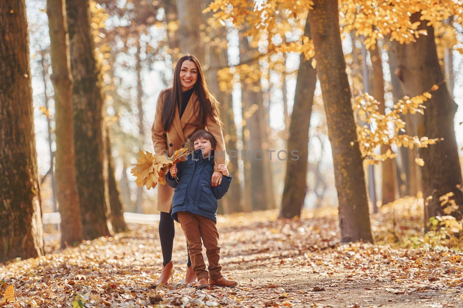 Front view. Mother with her son is having fun outdoors in the autumn forest by Standret