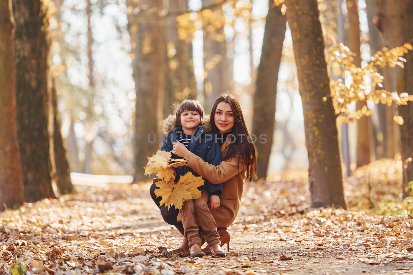 Front view. Mother with her son is having fun outdoors in the autumn forest.