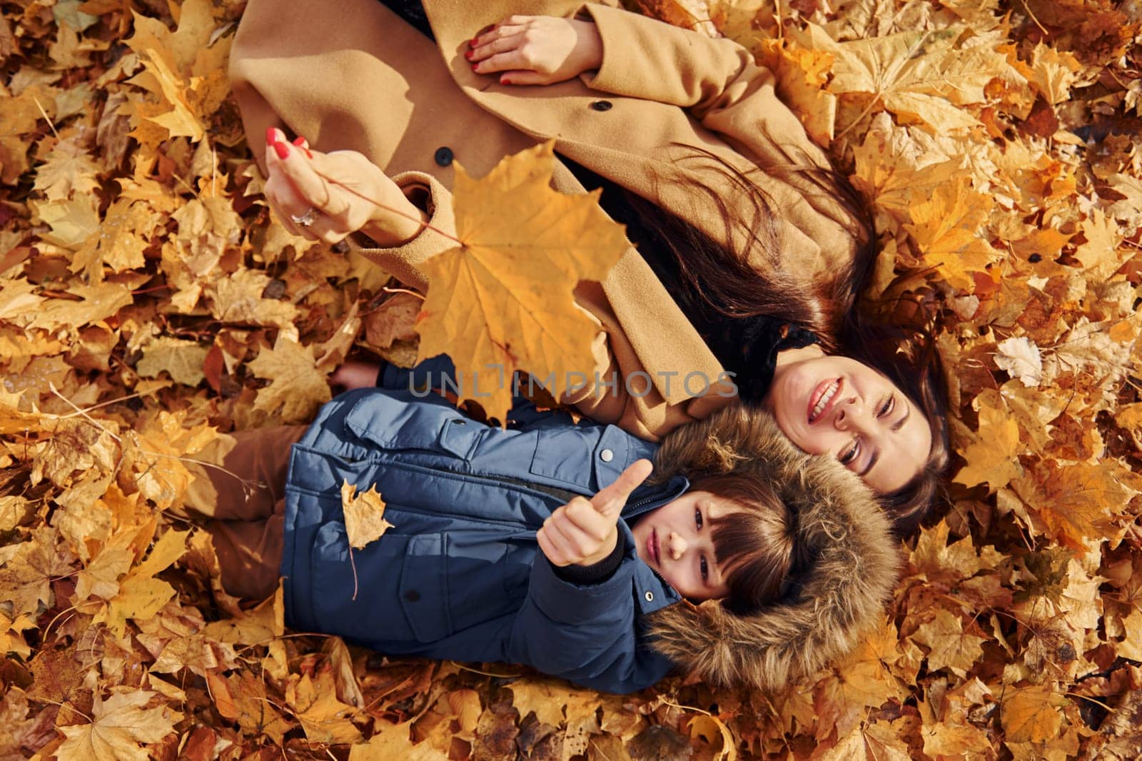 Laying down on the leaves. Mother with her son is having fun outdoors in the autumn forest.