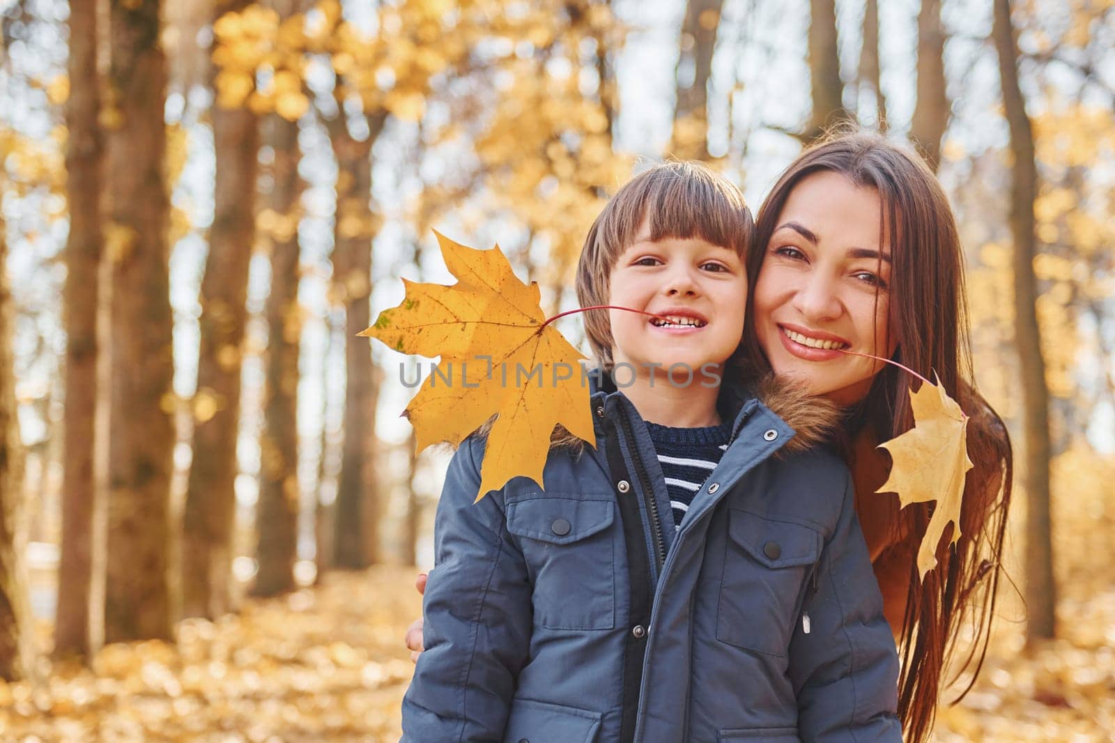 Mother with her son is having fun outdoors in the autumn forest.