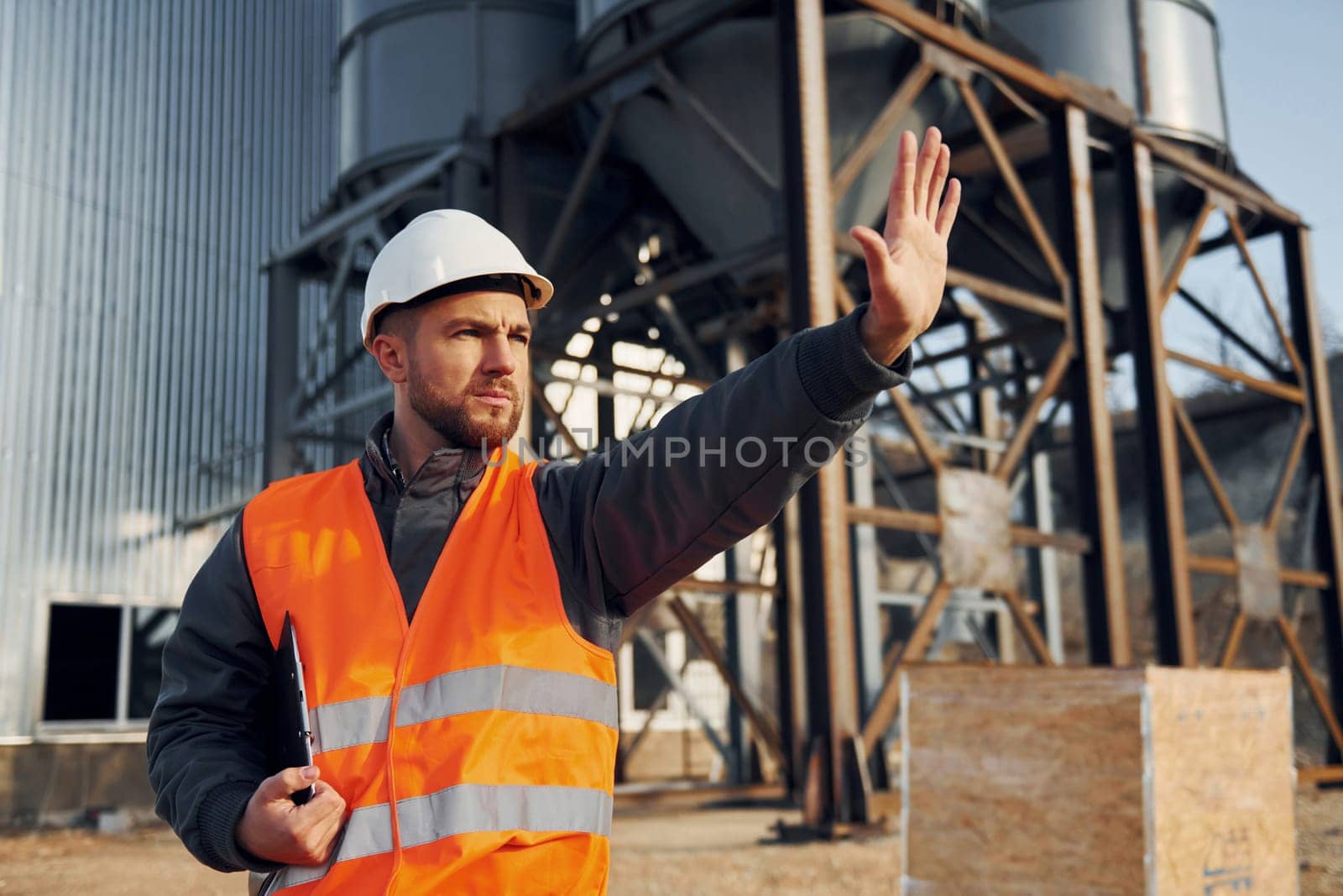 Showing stop gesture. Construction worker in uniform is outdoors near the factory.