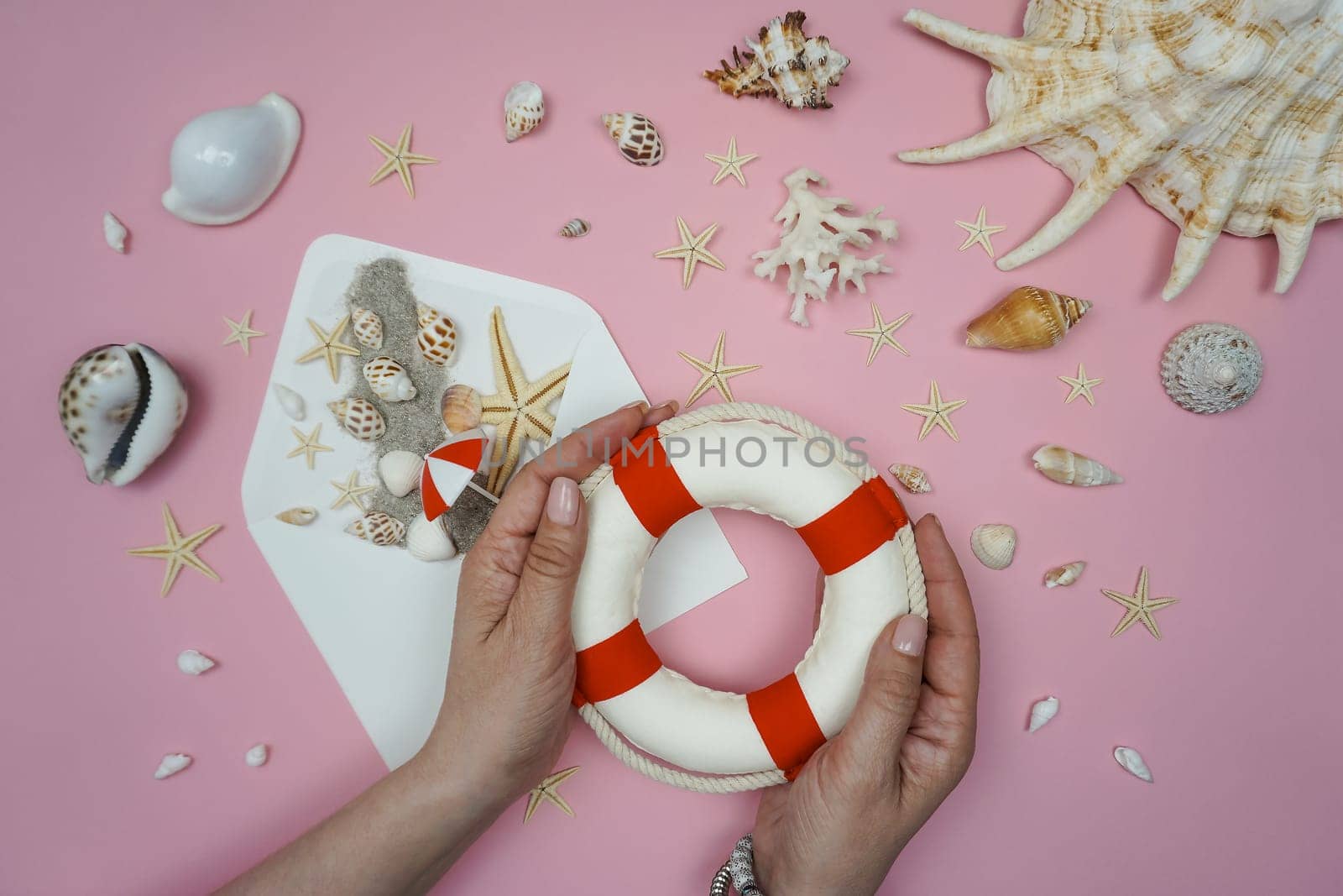 A lifebuoy in women's hands on a pink background with shells, starfish and memories of summer.