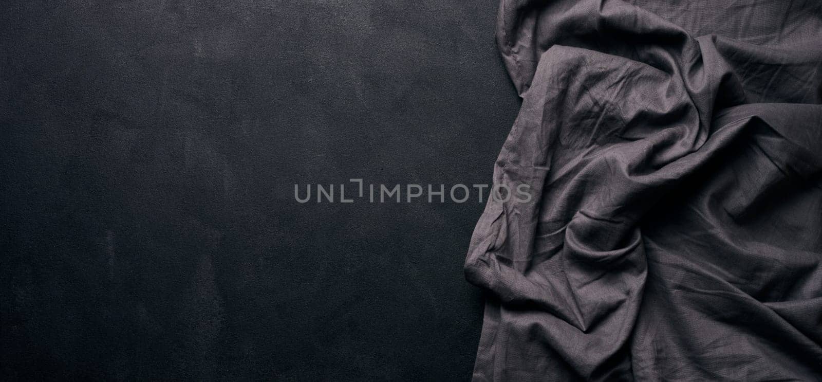 Folded black linen linen kitchen towel on a black background, top view. Copy space by ndanko