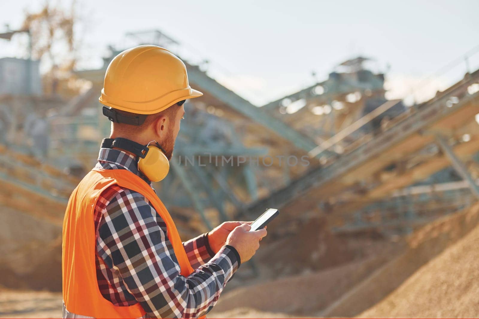 With yellow headphones on neck. Construction worker in uniform is on the quarry.