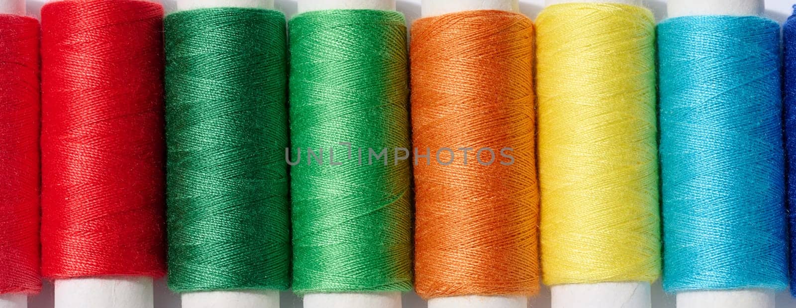 Multicolored spools of sewing threads on a white background, top view by ndanko