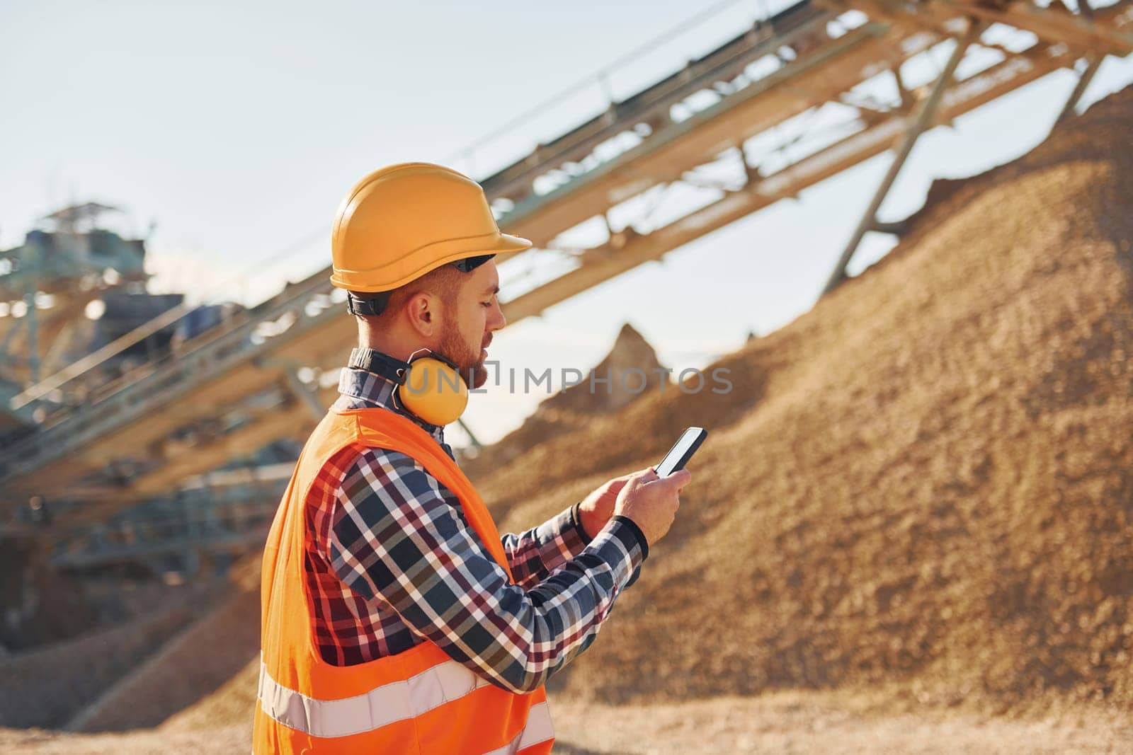 With yellow headphones on neck. Construction worker in uniform is on the quarry.