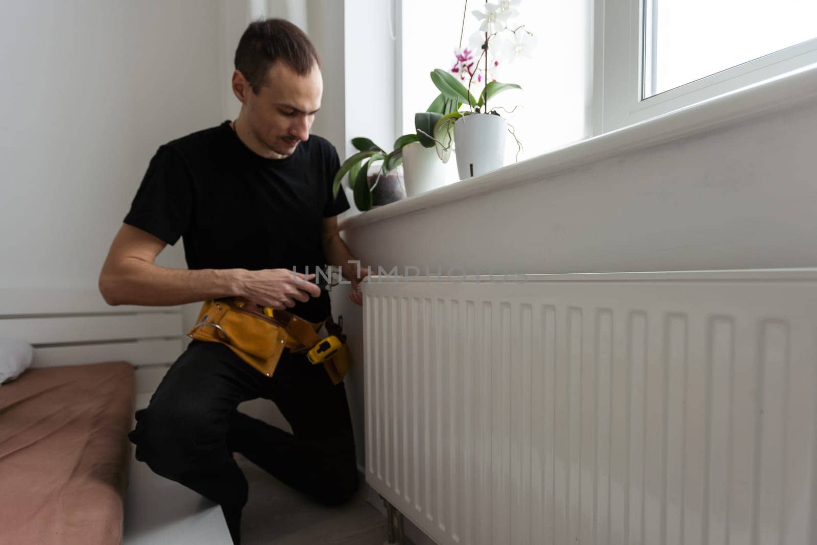 Man is repairing radiator battery in the room. Maintenance repair works renovation in the flat. Heating restoration. Wrench in hands by Andelov13