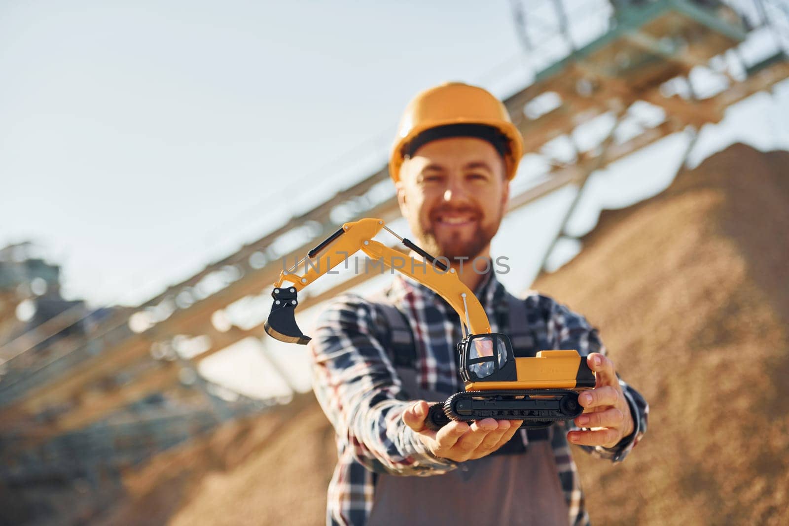 Holding toy. Construction worker in uniform is on the quarry.