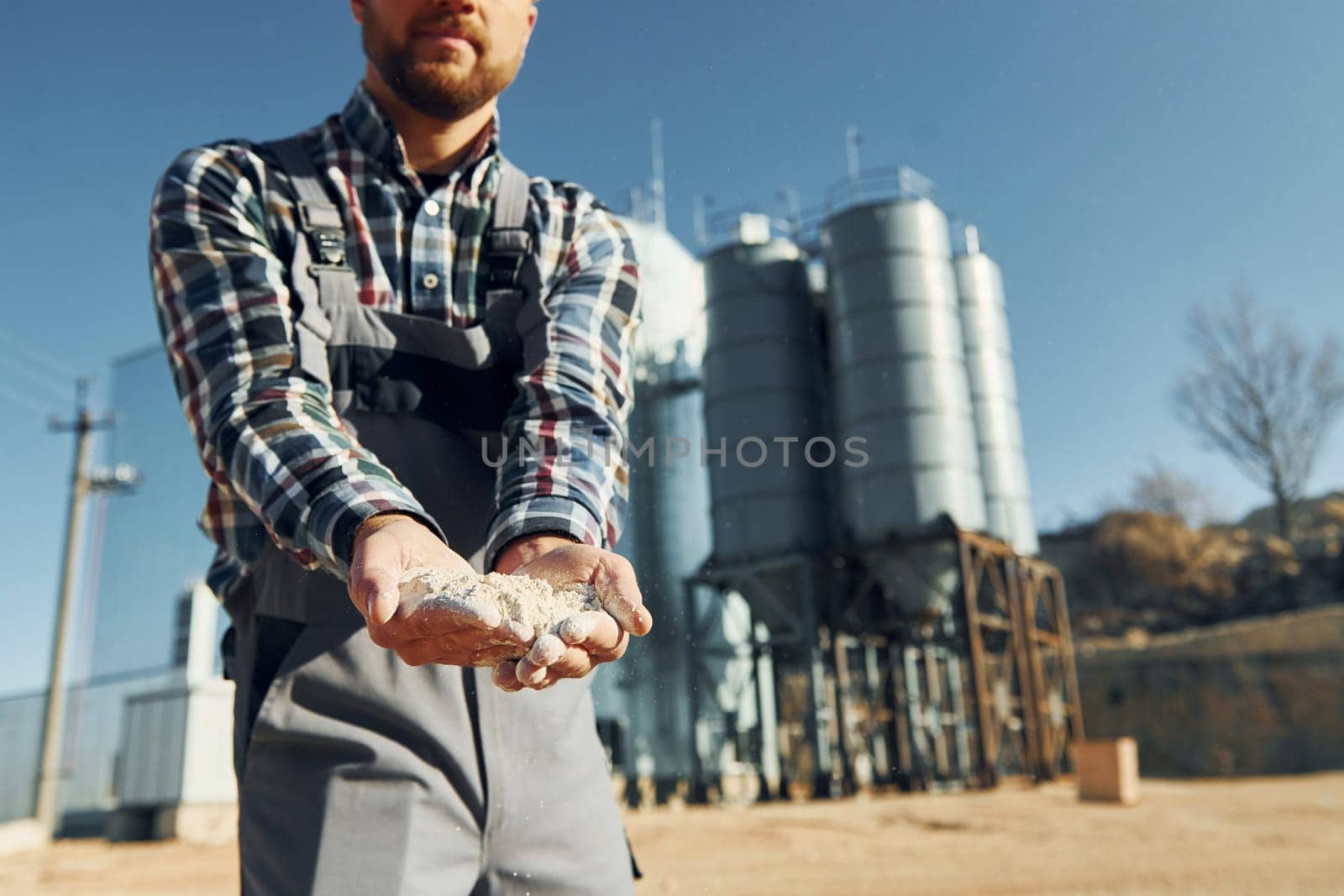 Holding soil. Construction worker in uniform is outdoors near the factory.