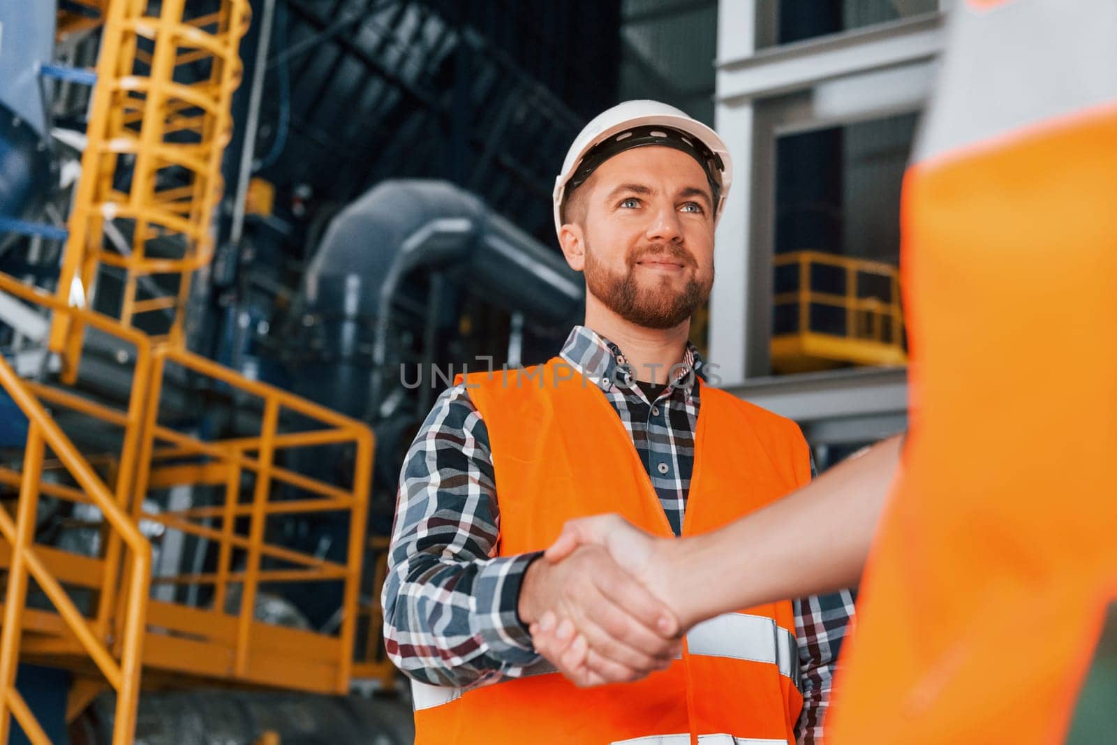 Making handshake with customer. Construction worker in uniform is in the factory.