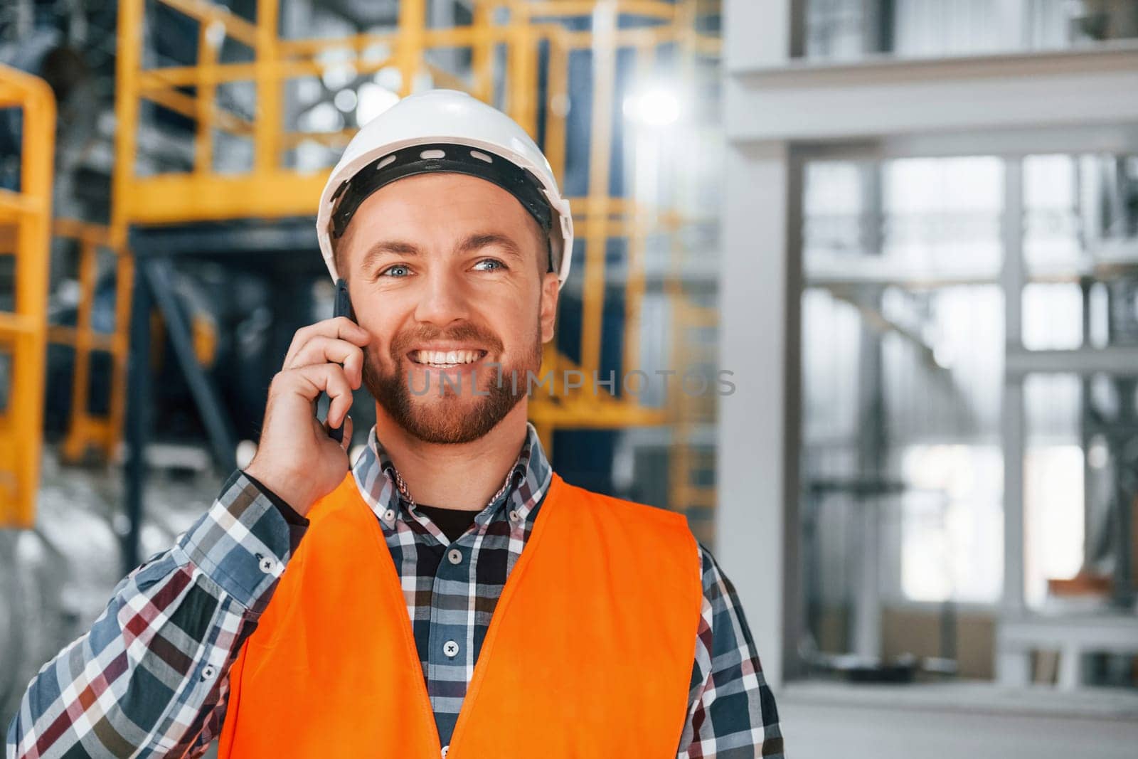 Talking by phone. Construction worker in uniform is in the factory.