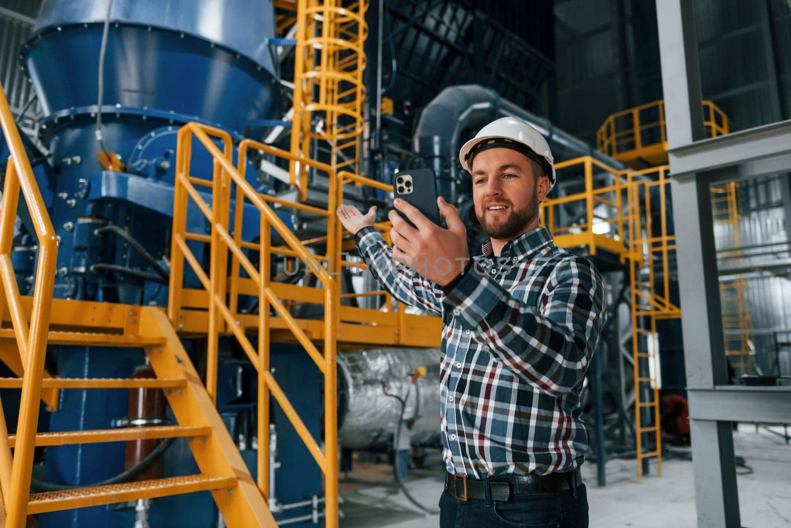 Holding phone. Construction worker in uniform is in the factory.