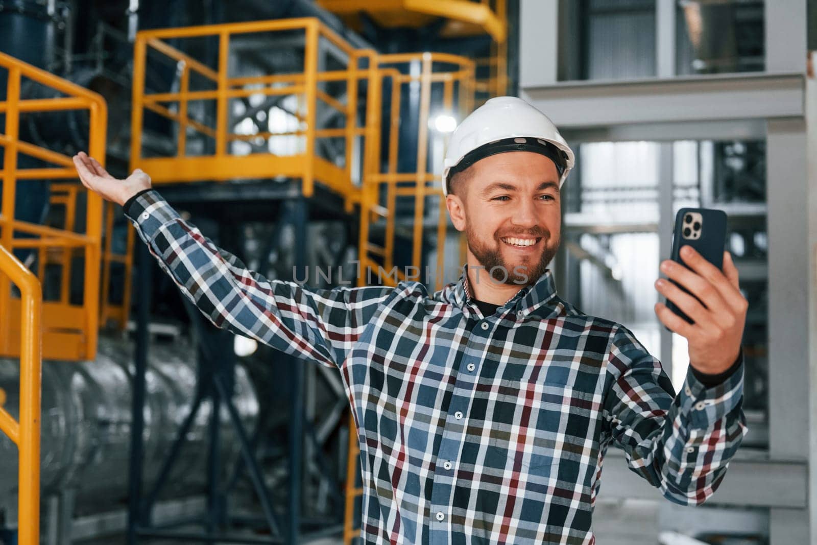 Holding phone. Construction worker in uniform is in the factory.