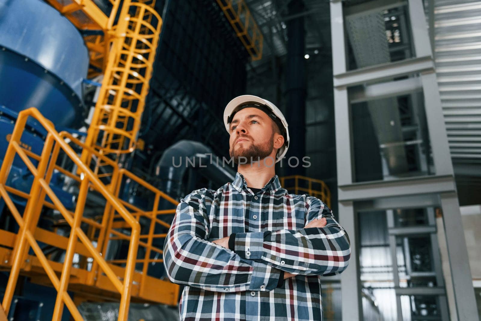 Standing with arms crossed. Construction worker in uniform is in the factory.