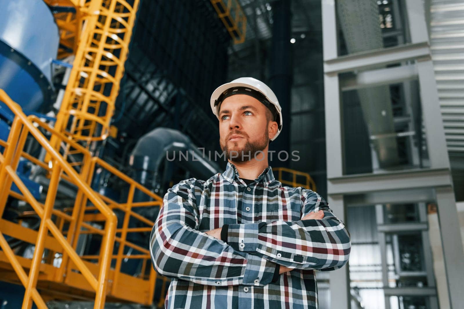 Standing with arms crossed. Construction worker in uniform is in the factory.
