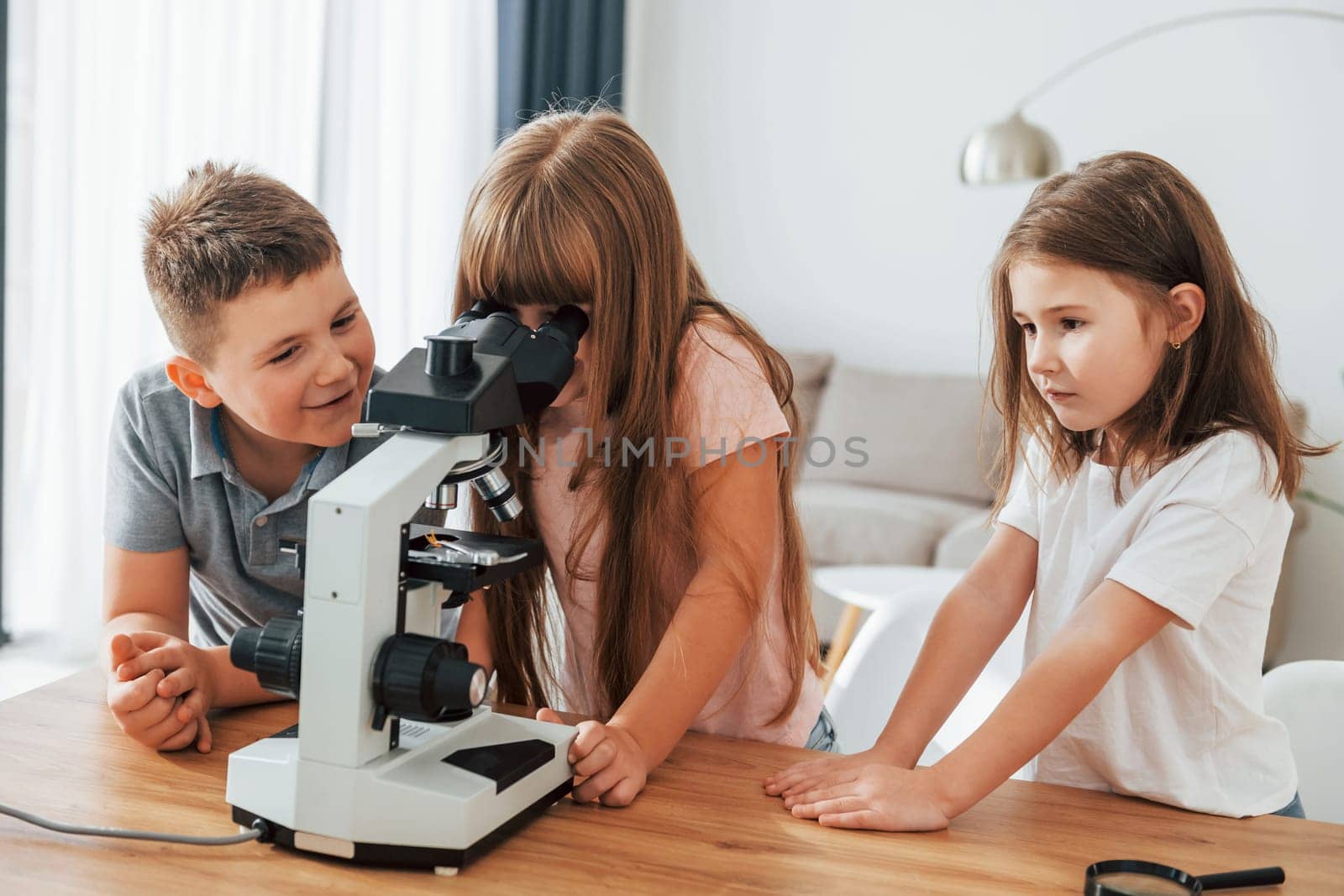 Using microscope. Kids having fun in the domestic room at daytime together.