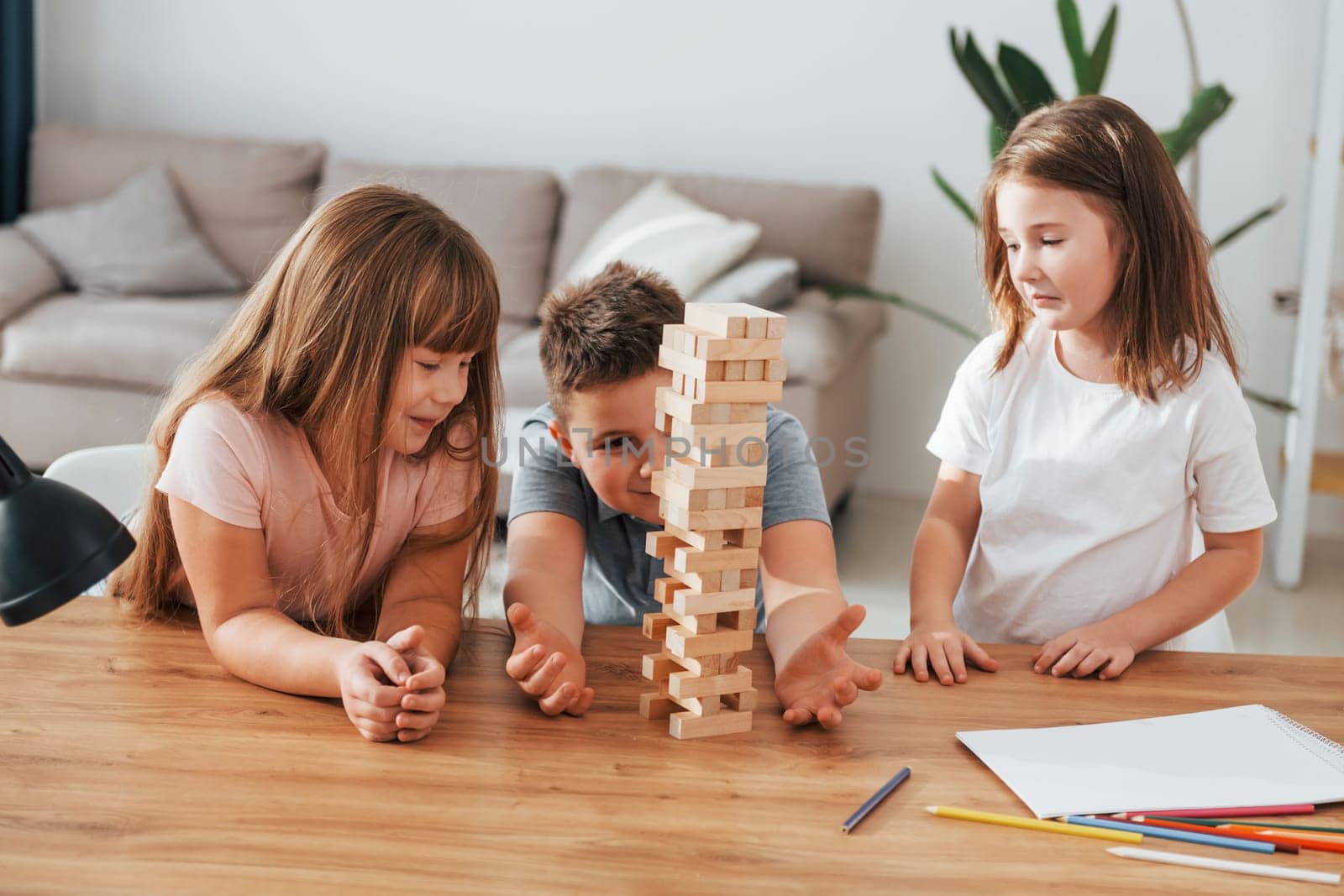 Jumbling tower game. Kids having fun in the domestic room at daytime together.