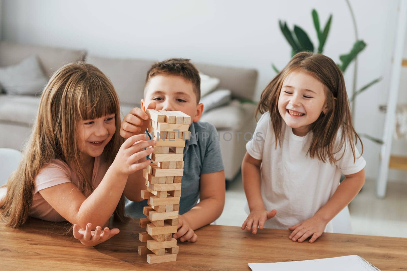Jumbling tower game. Kids having fun in the domestic room at daytime together.