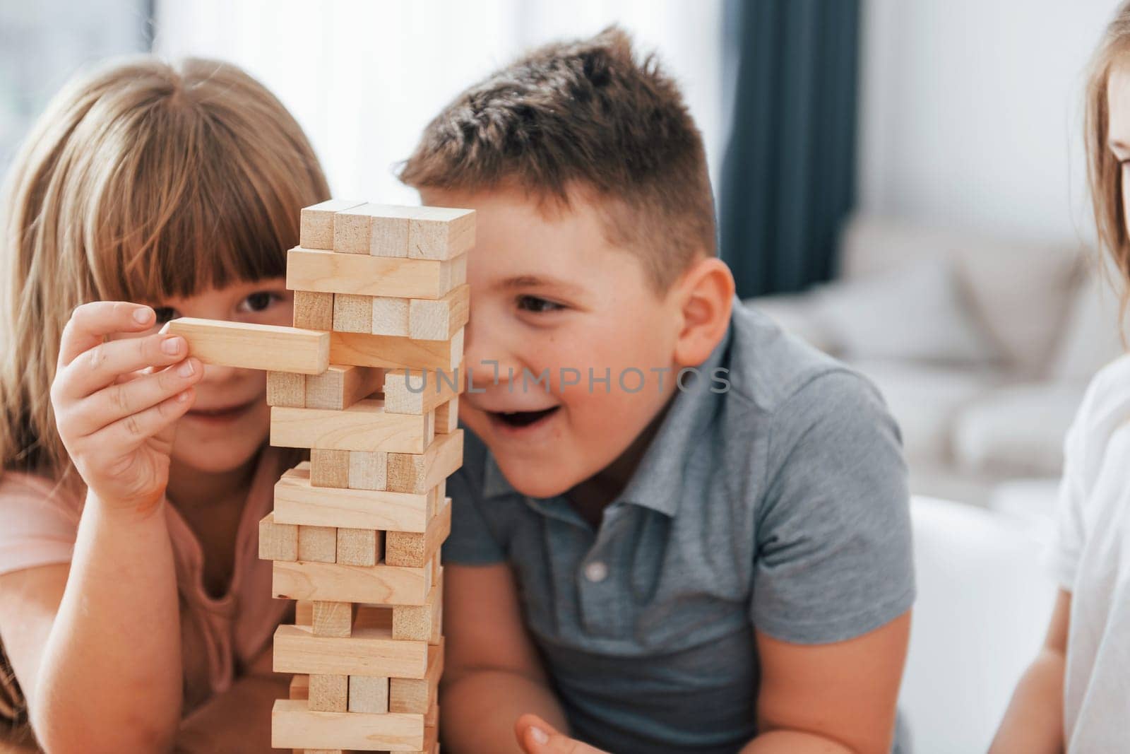 Jumbling tower game. Kids having fun in the domestic room at daytime together.