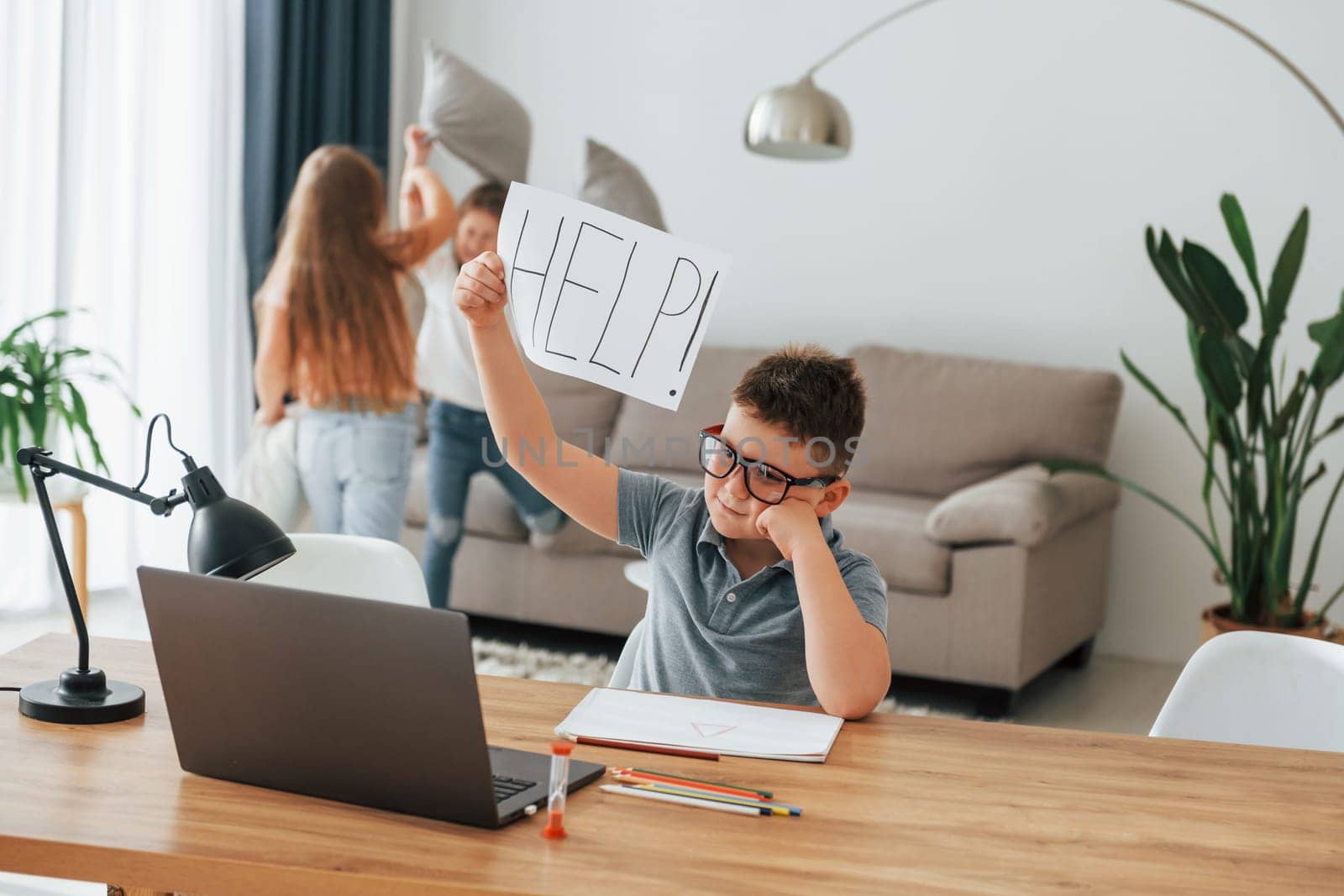Boy holding paper with help word. Refuses to take a lesson. Kids having fun in the domestic room at daytime together.