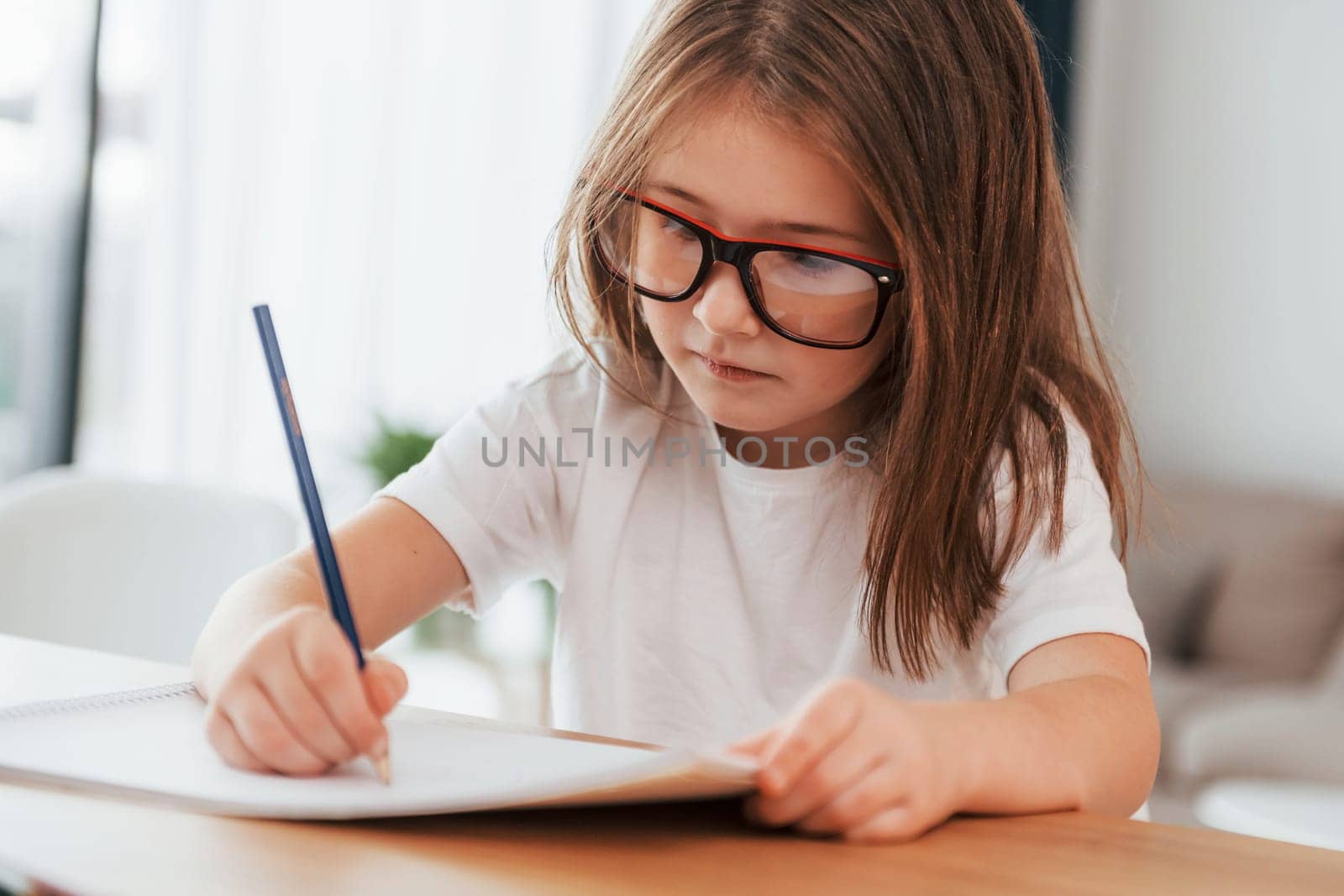 Little girl is sitting by the table and learning to draw.