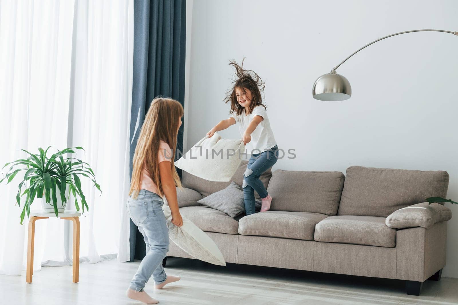 Running with pillows. Kids having fun in the domestic room at daytime together.