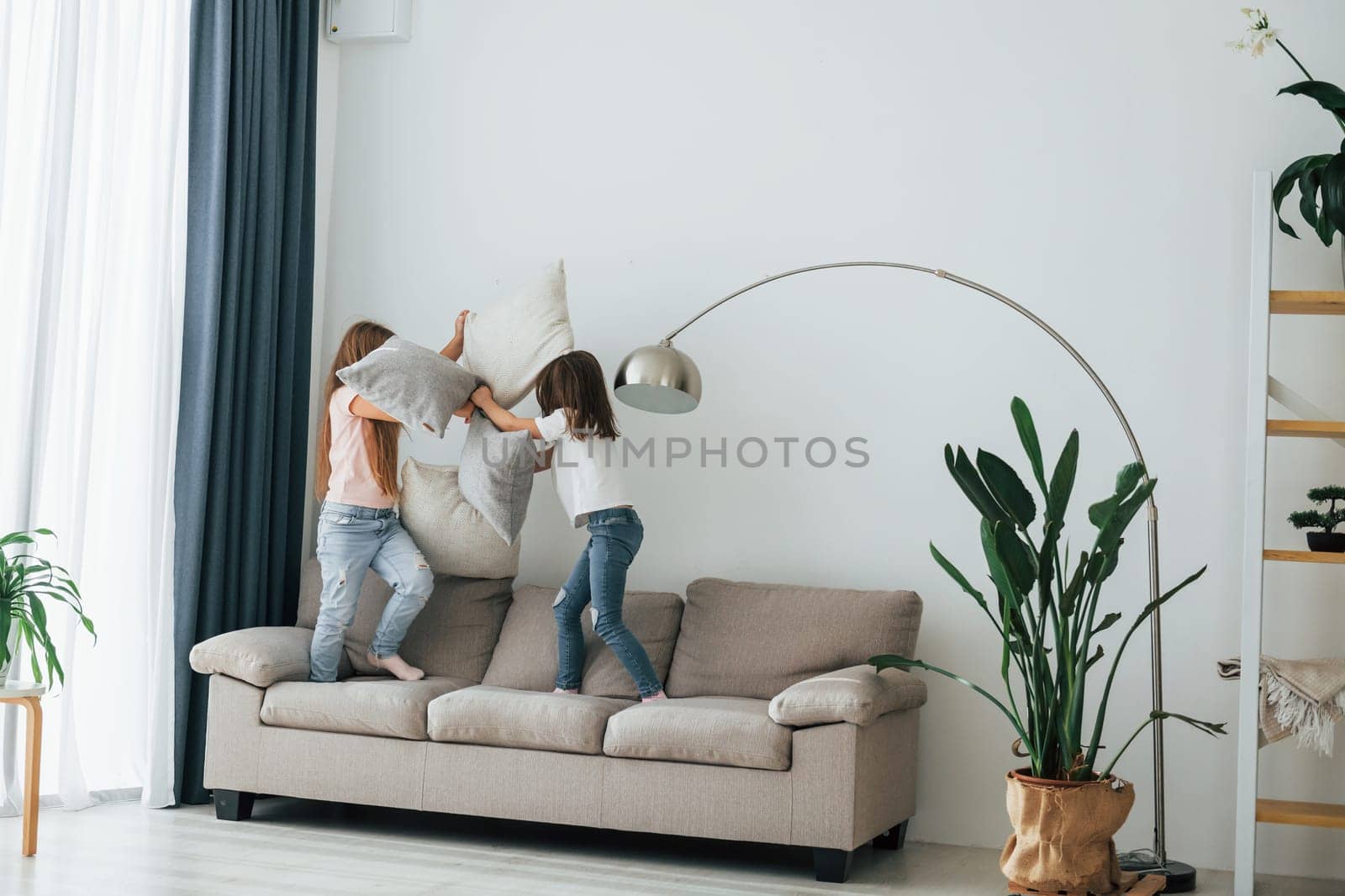 Running with pillows. Kids having fun in the domestic room at daytime together.