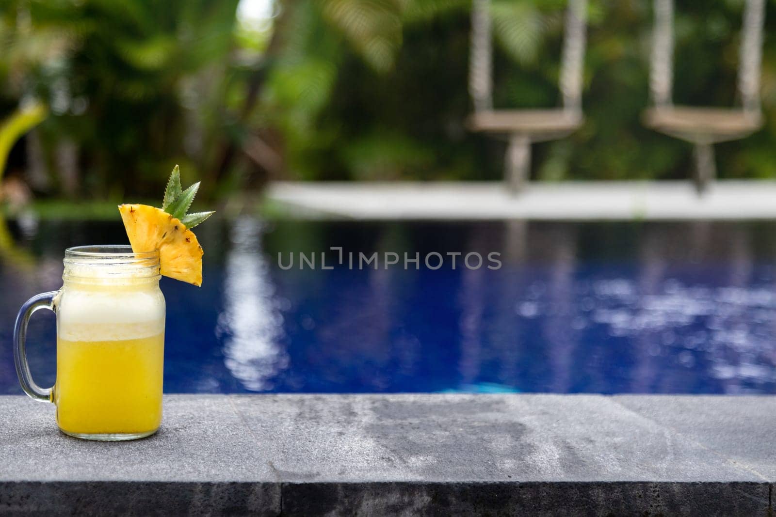 Fresh pineapple juice on swimming pool ledge on tropical paradise vacation resort. Copy space. No people. Vacation lifestyle concept.