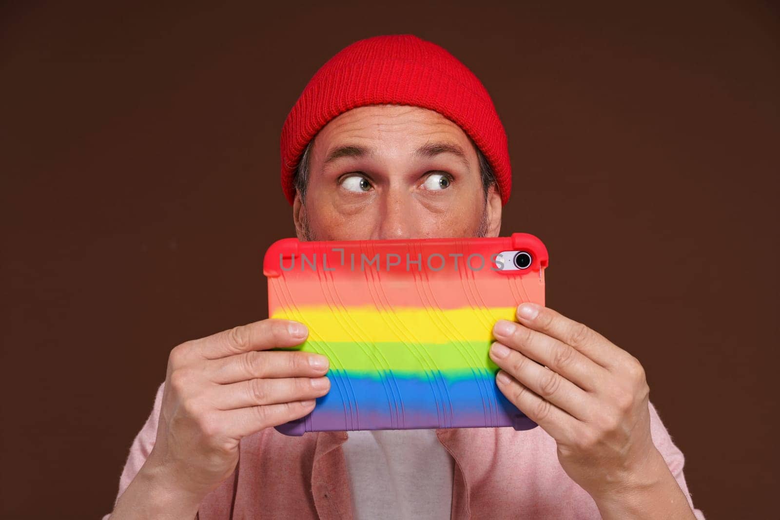 Gay man depicted feeling ashamed sexual orientation online, looking out with fear over tablet LGBT coloring. man in digital world represents negative emotions associated with secrecy and hidden personal identity. by LipikStockMedia