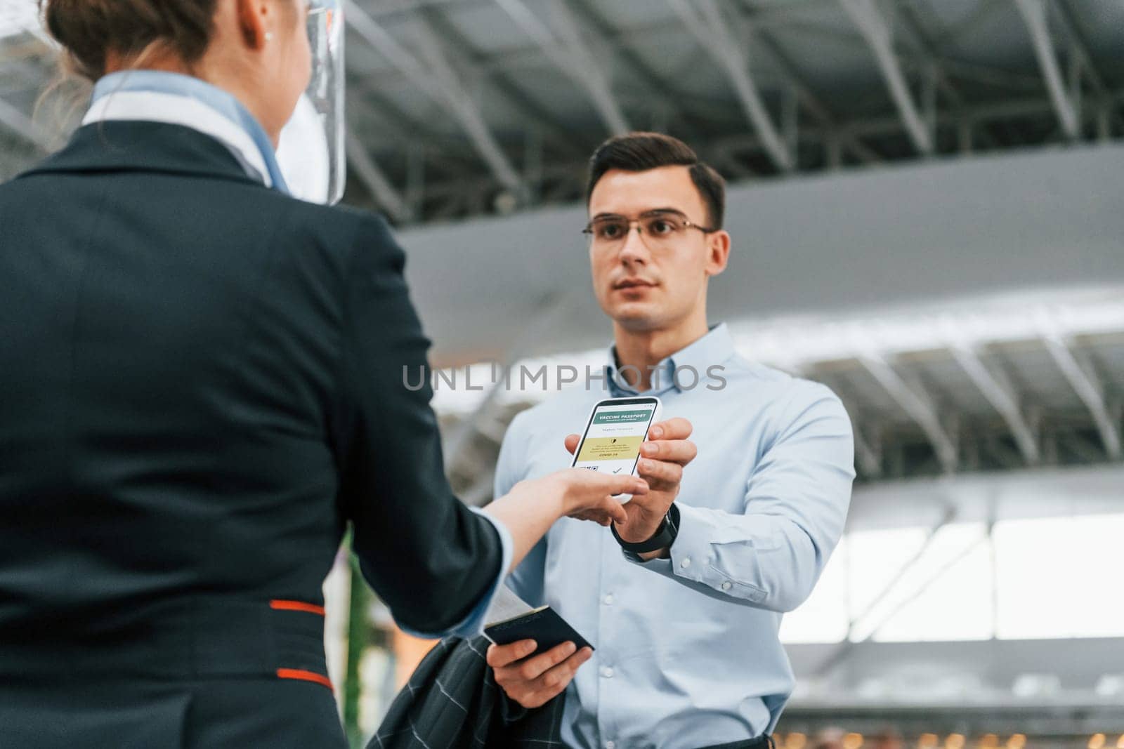 Man showing vaccination certificate. Young businessman in formal clothes is in the airport at daytime by Standret