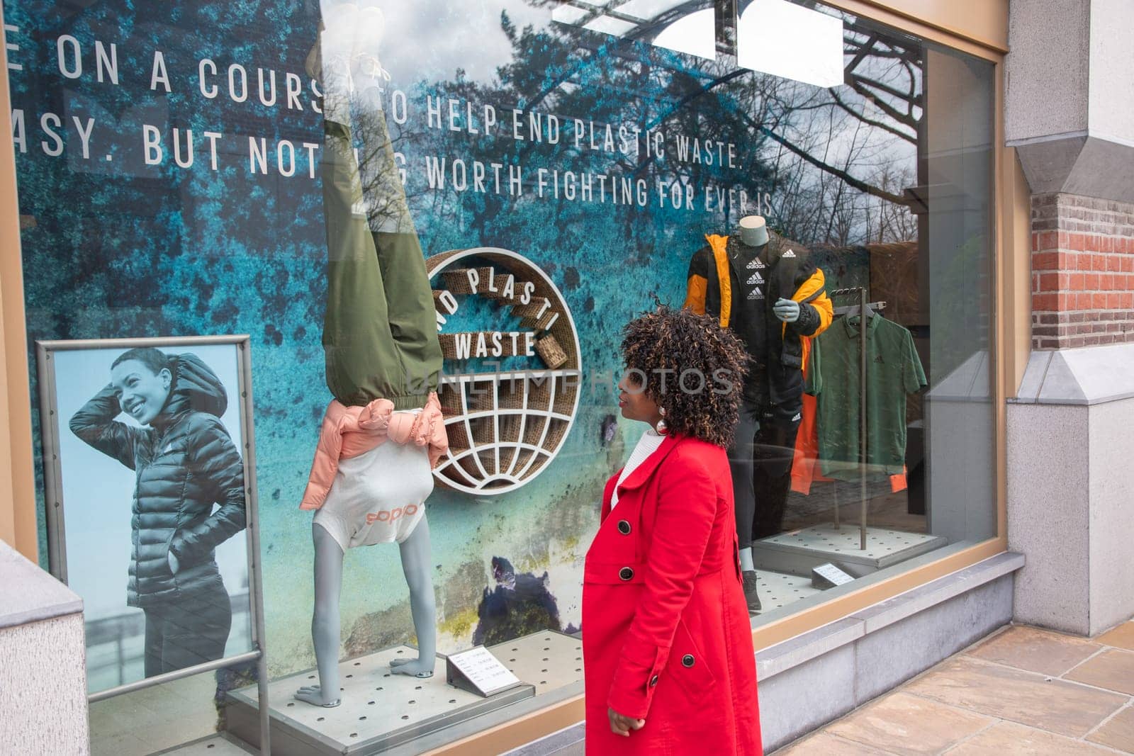 an African American woman looks at a shop window at a poster calling for not littering the earth with plastic waste, Maasmechelen, Belgium,February 17,2023. High quality photo