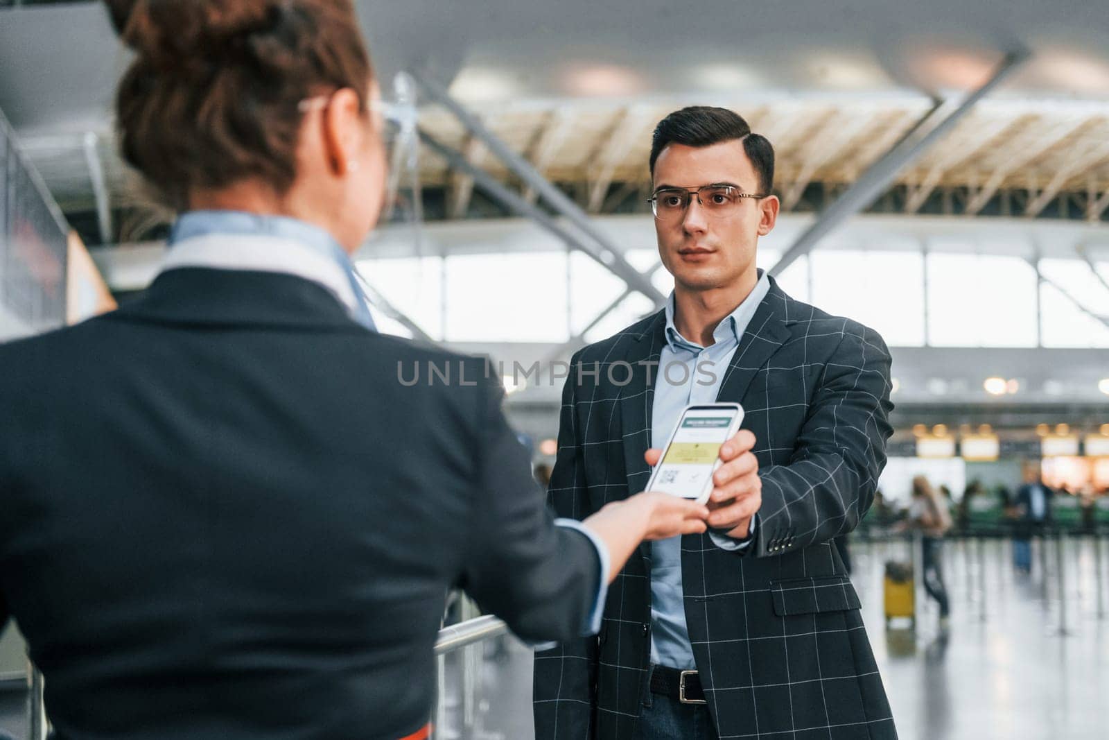 Holding and showing vaccination certificate. Young businessman in formal clothes is in the airport at daytime.