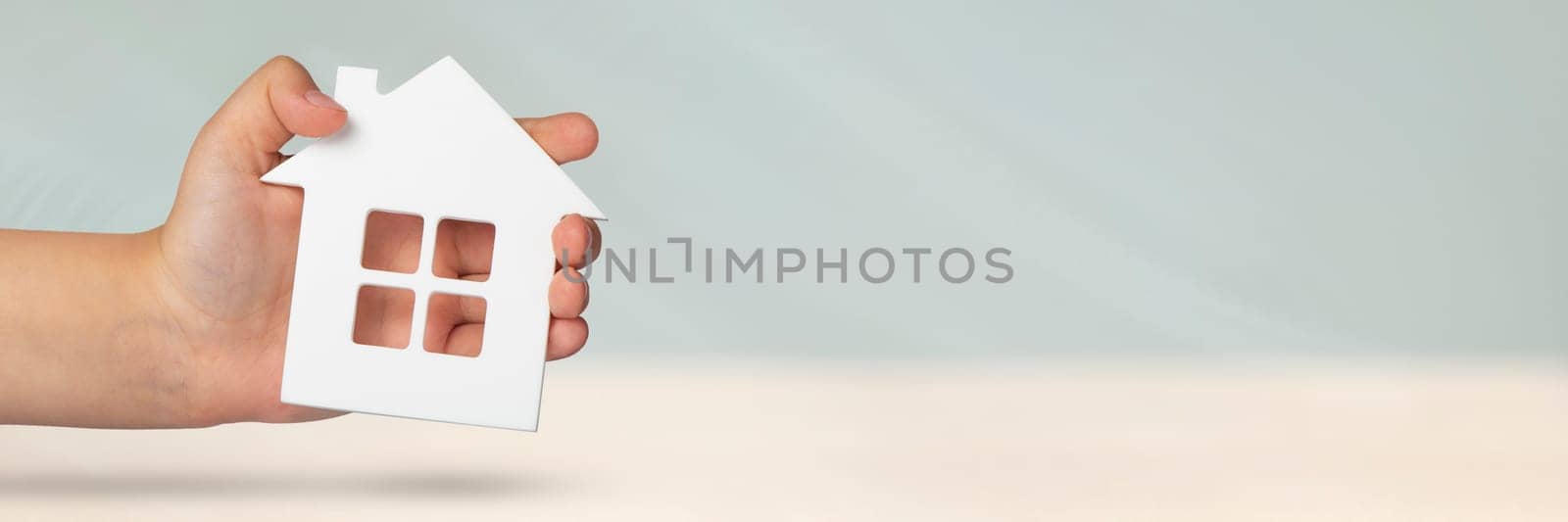 Real estate insurance. Model of a white house in hands on a gray blurred background. Insure a house or apartment, the concept of insurance services, with copy space.