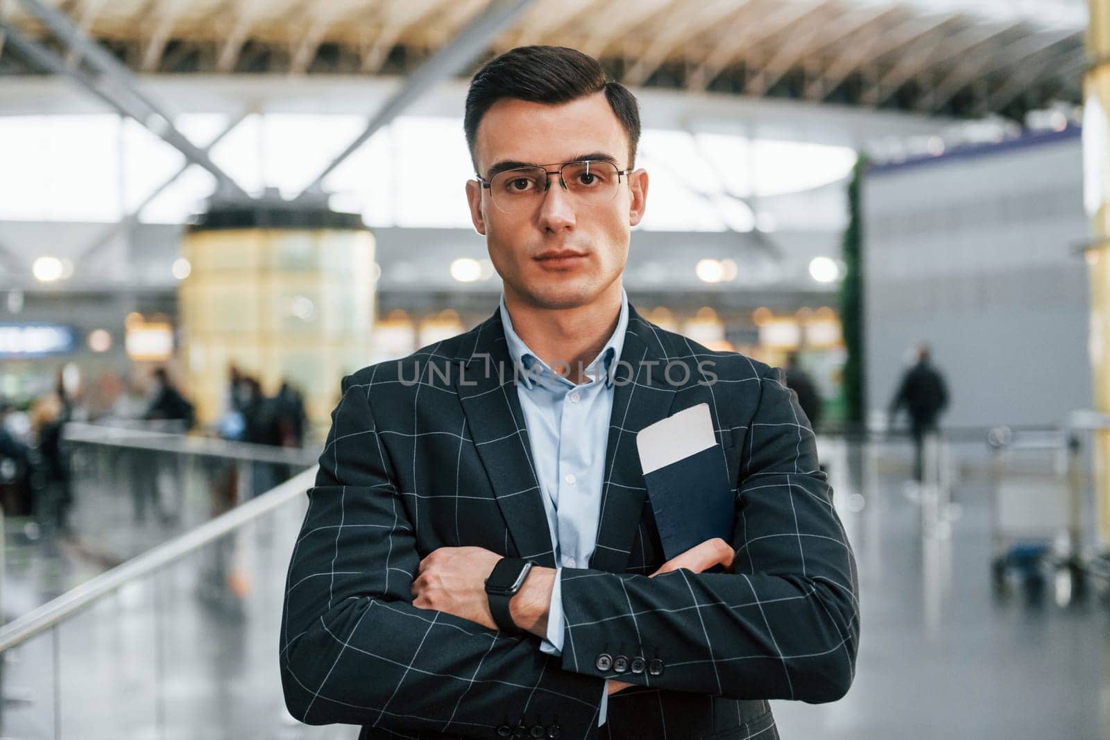 With arms crossed. Young businessman in formal clothes is in the airport at daytime.