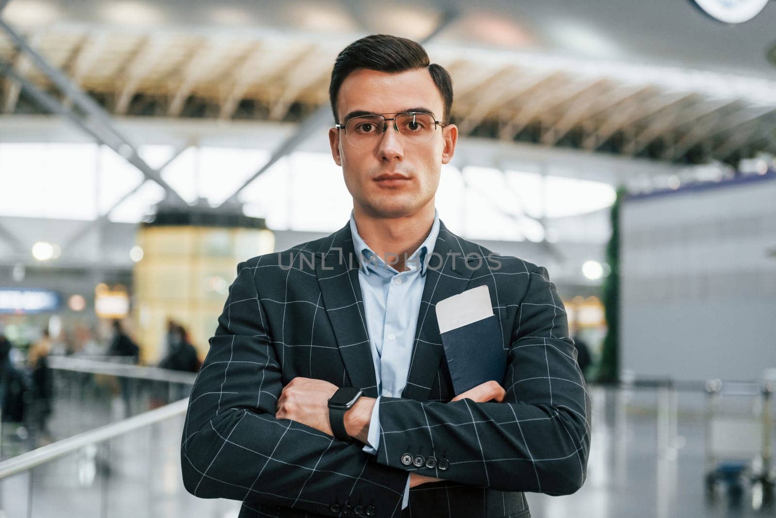 With arms crossed. Young businessman in formal clothes is in the airport at daytime.