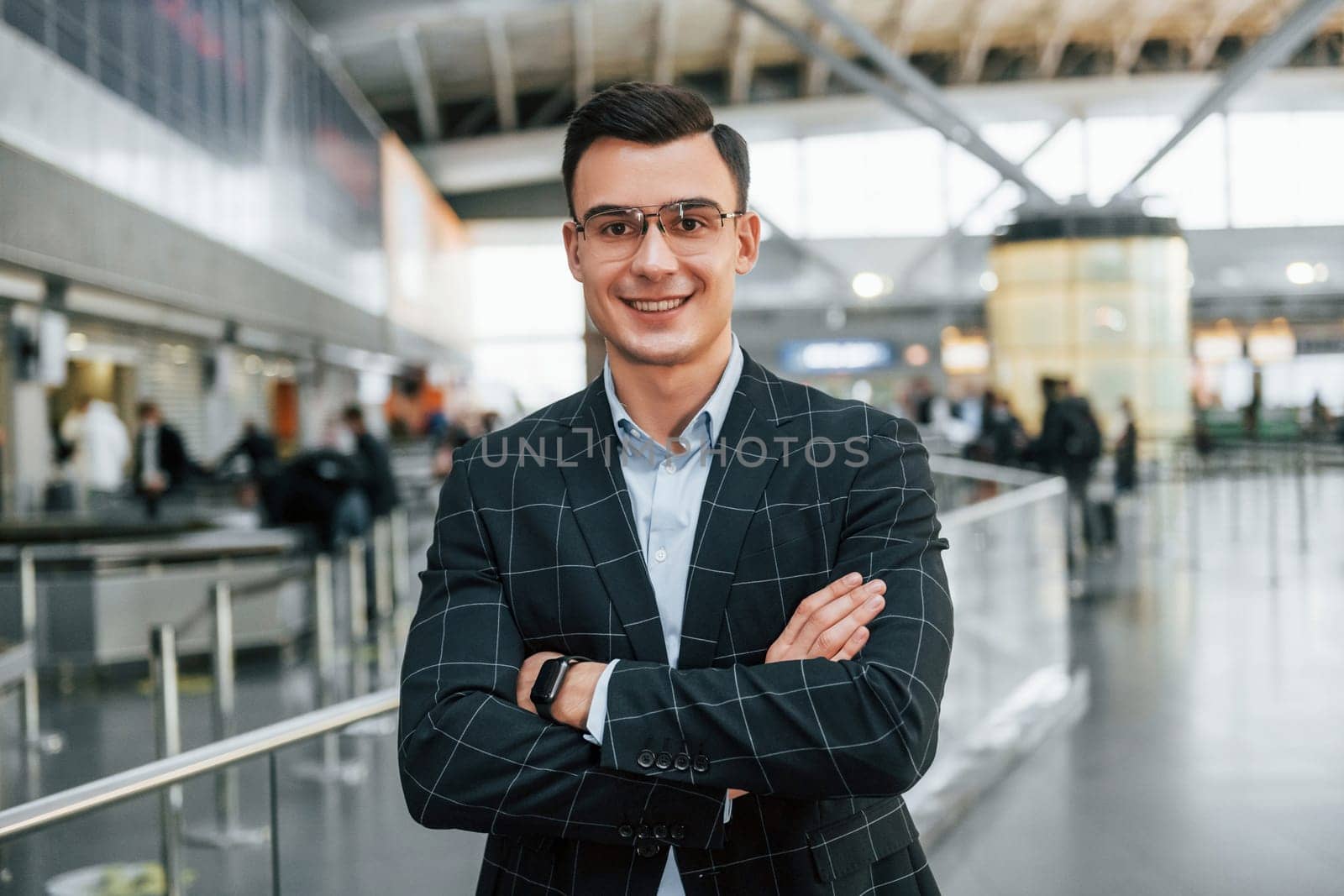 With arms crossed. Young businessman in formal clothes is in the airport at daytime.