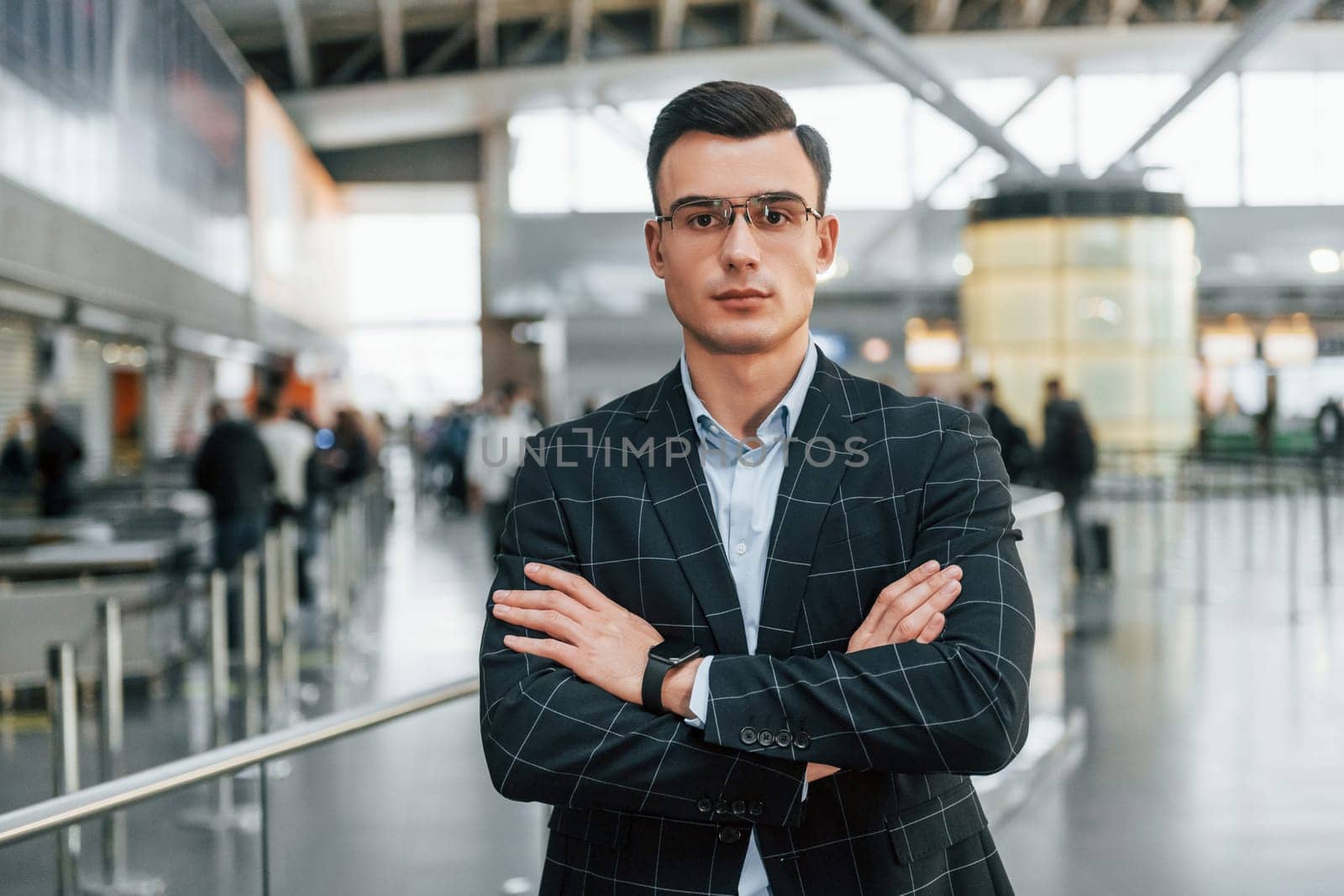 With arms crossed. Young businessman in formal clothes is in the airport at daytime.