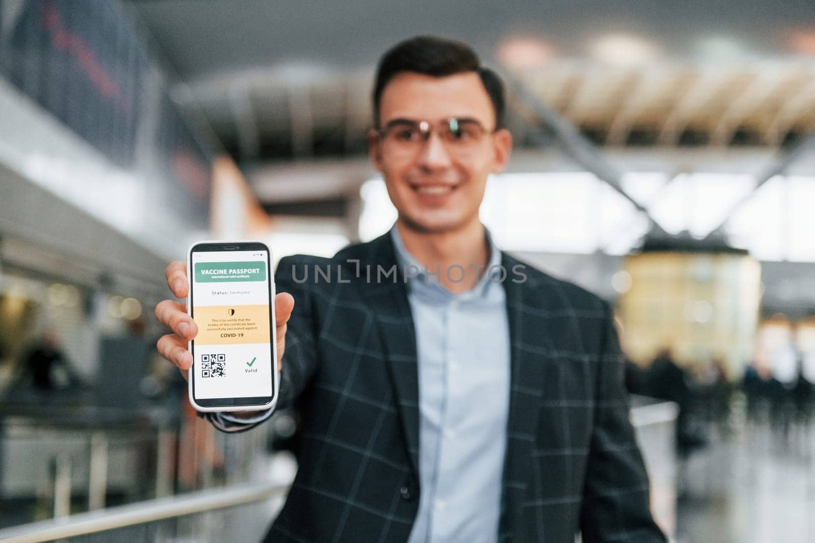 With vaccination certificate. Young businessman in formal clothes is in the airport at daytime.