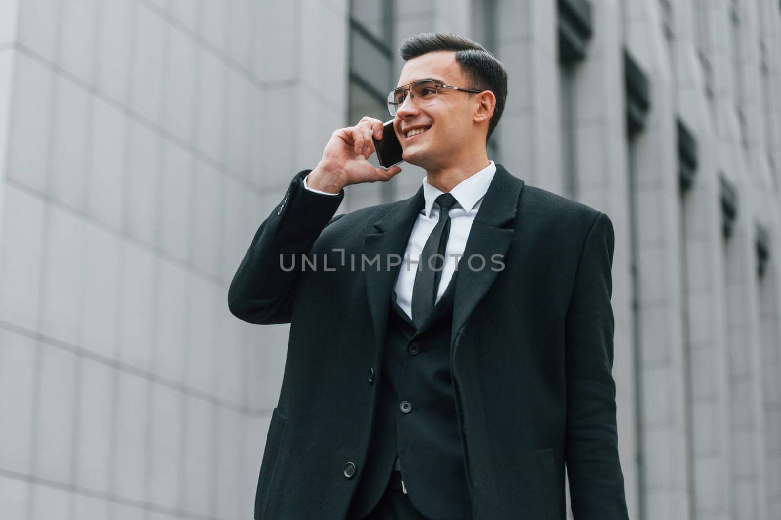 With smartphone. Businessman in black suit and tie is outdoors in the city.