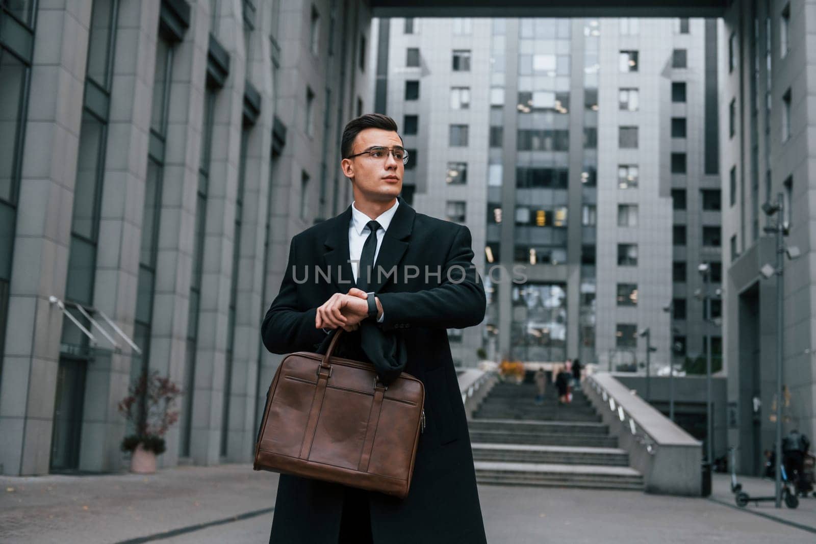 Front view. Businessman in black suit and tie is outdoors in the city.