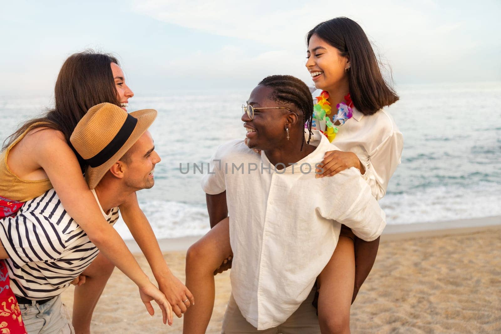 Happiness and friendship. Young multiracial friends having fun outdoors in the beach near ocean. Piggy back ride. Lifestyle concept.