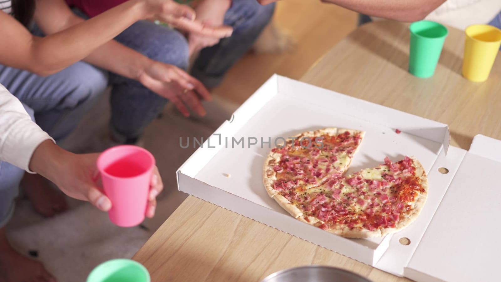 Slow motion video of a piece of pizza into a delivery box on the table with people around