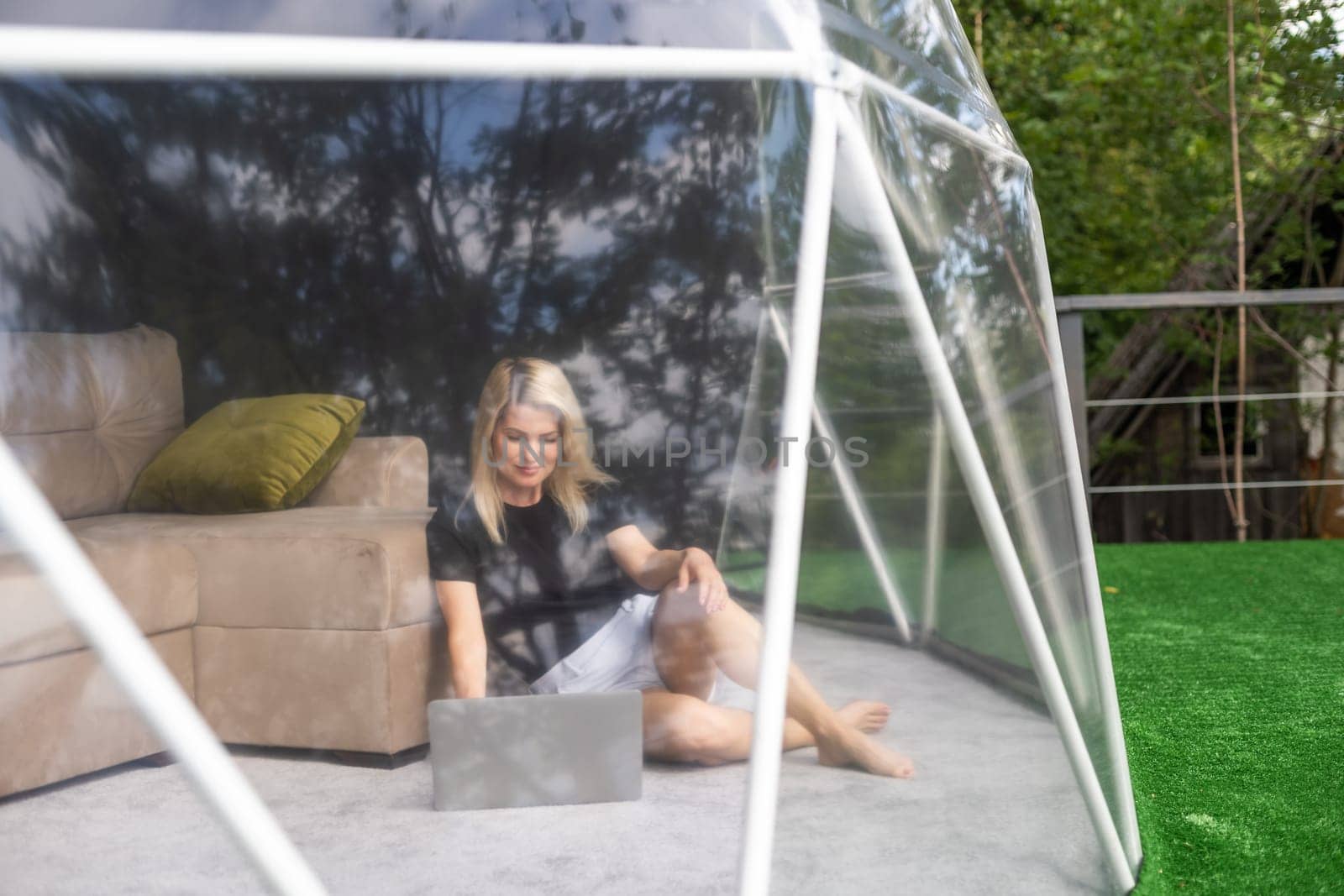 middle aged woman uses a laptop resting and spending time at Glamping house on holidays. holiday dome tent. Cozy, camping, hygge, lifestyle concept.