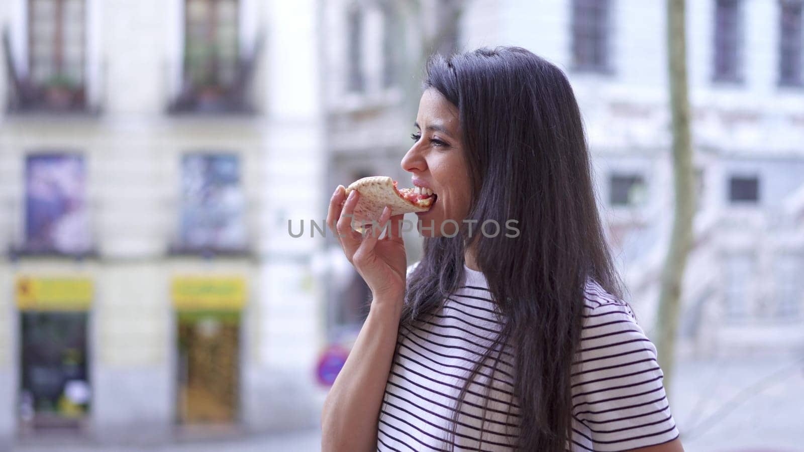 Slow motion video of a woman eating pizza and then smiling at camera in a balcony