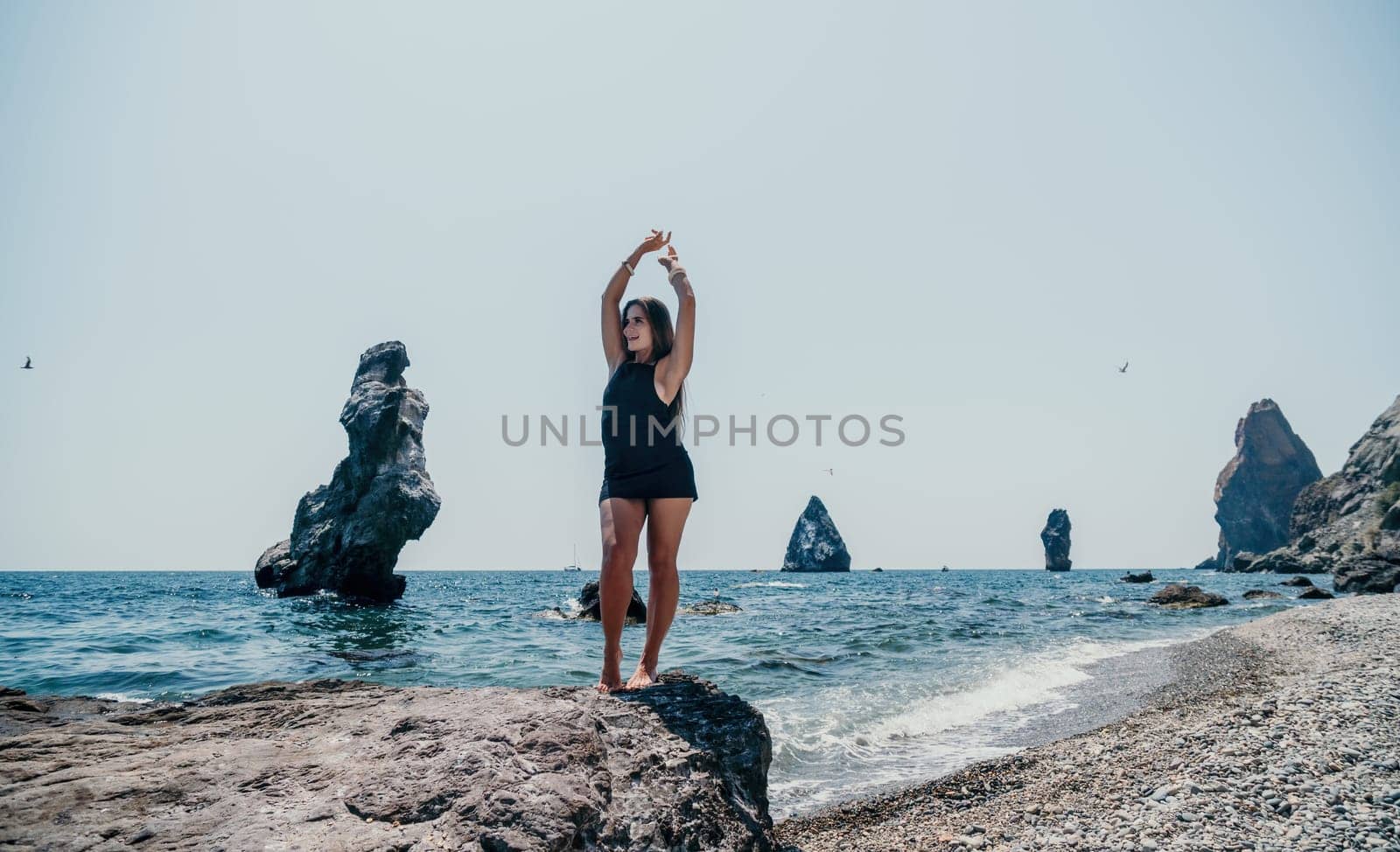 Woman travel sea. Young Happy woman in a long red dress posing on a beach near the sea on background of volcanic rocks, like in Iceland, sharing travel adventure journey