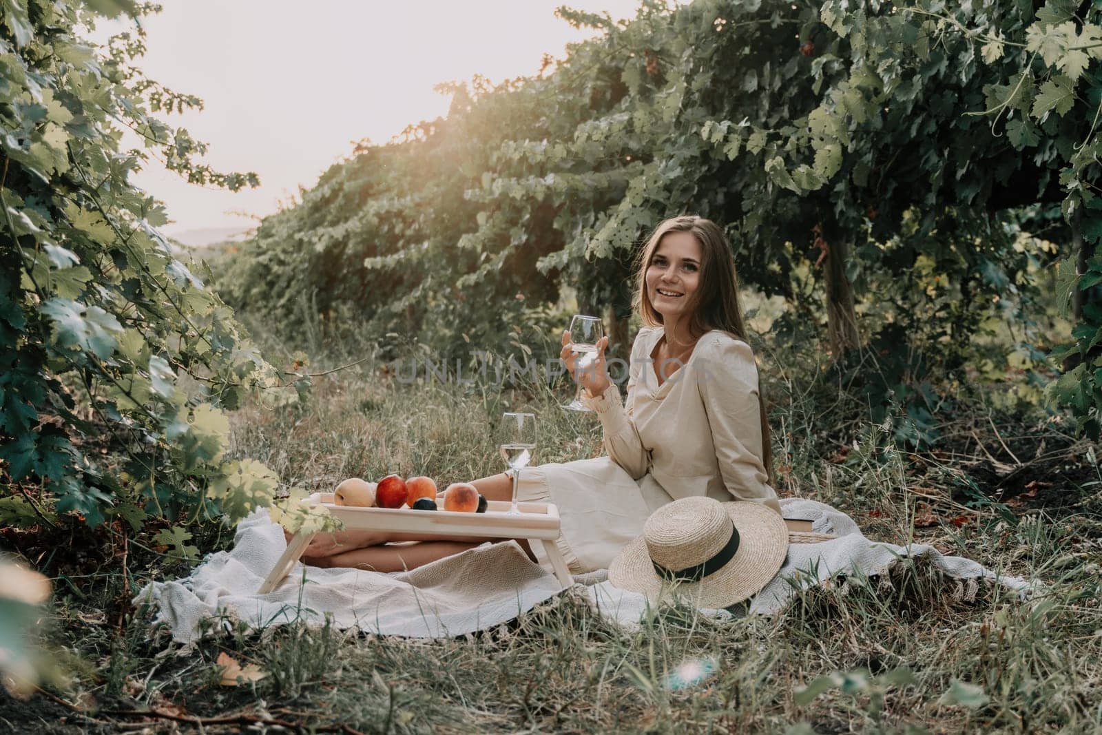 Woman picnic vineyard. Happy woman with a glass of wine at a picnic in the vineyard, wine tasting at sunset and open nature in the summer. Romantic dinner, fruit and wine. by panophotograph