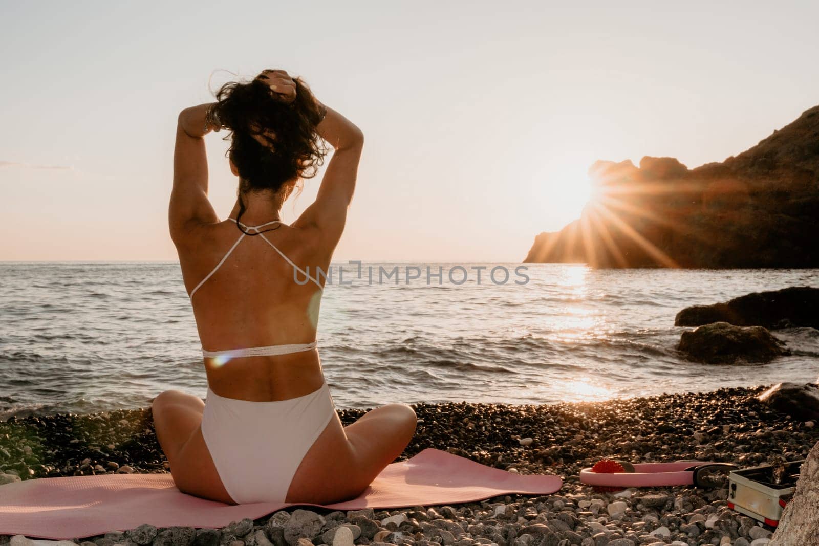 Woman sea yoga. Happy woman in white swimsuit and boho style braclets practicing outdoors on yoga mat by sea on sunset. Women yoga fitness routine. Healthy lifestyle, harmony and meditation by panophotograph