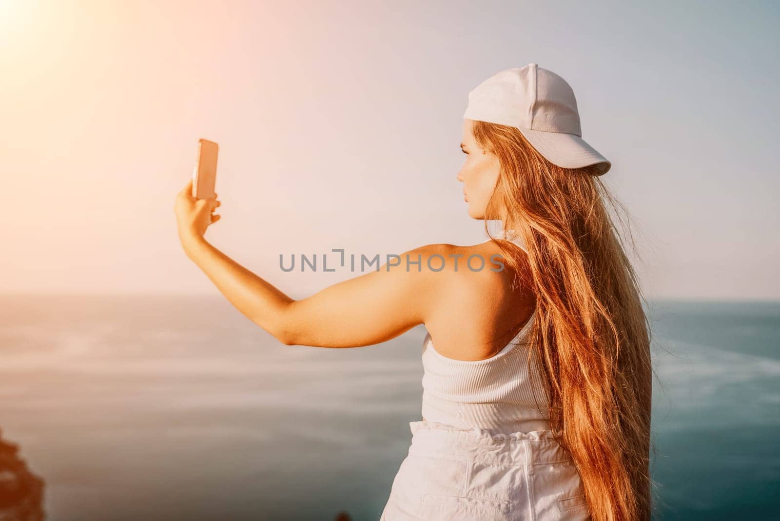 Woman travel sea. Happy tourist in hat enjoy taking picture outdoors for memories. Woman traveler posing on the beach at sea surrounded by volcanic mountains, sharing travel adventure journey by panophotograph